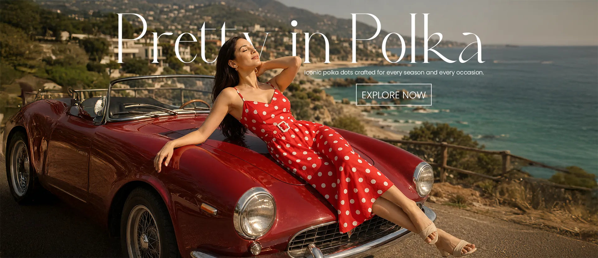 Red polka dot midi dress featured in a luxury fashion campaign with a vintage car and ocean-view backdrop, highlighting timeless women's summer style.